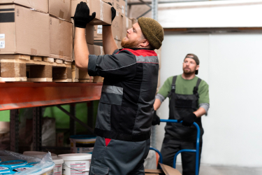 Muž ťahá krabicu z regálu na pripravený vozík Muž ťahá krabicu z regálu na pripravený vozík