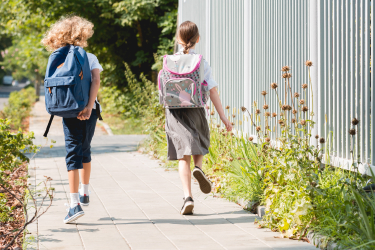 Dve dievčatá s aktovkami idú po chodníku