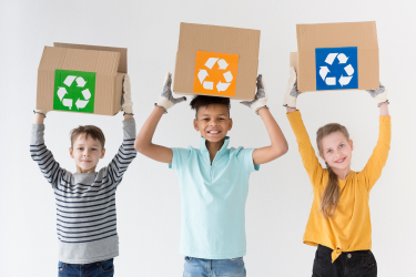 Tri deti s papierovými krabicami nad hlavou so symbolmi recyklácie