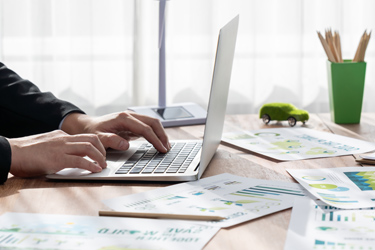 Človek pracuje na notebooku a okolo seba má veľa grafov Človek pracuje na notebooku a okolo seba má veľa grafov