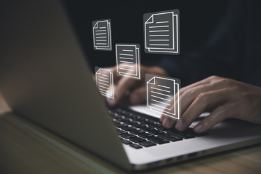 Človek píše na klávesnici notebooku, nad ktorým poletujú súbory